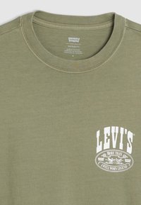 Olive green cotton t-shirt with a round neckline and short sleeves. Features a prominent white Levi's logo graphic on the chest.
