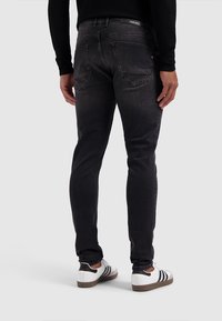 Zwarte denim jeans met een slim fit, voorzien van achterzakken, subtiele vervaging en een lichte rek. Gepaard met witte sneakers en een zwarte top.