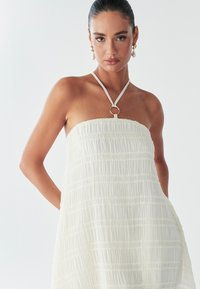 Strapless witte jurk van textuurstof met een geplooid ontwerp, met een cirkelvormige ringaccent bij de halslijn.
