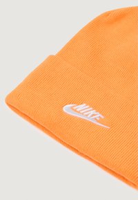 Căciulă tricotată de un portocaliu strălucitor cu logo-ul Nike brodat alb pe marginea pliată, pe un fundal simplu.