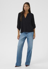 Top noir à manches longues avec un col en V et des manches retroussées, associé à un jean bleu clair à jambes larges. Tissu doux et coupe décontractée.