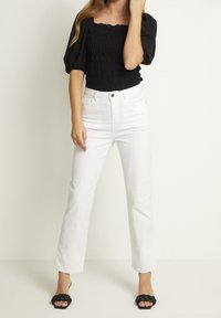 Top negro con fruncido y mangas cortas abullonadas, combinado con jeans blancos de pierna recta de cintura alta y sandalias planas trenzadas negras.