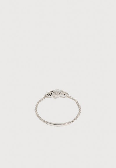 Bague chaîne en argent délicate avec un détail de barre fine courbée et un petit groupe de formes géométriques sur fond blanc.