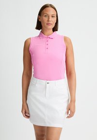Rosa ärmlös polo-topp med krage och framknäppning, kombinerad med en vit denimkjol med framficka och lätt fåll.