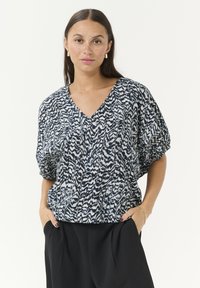 Blouse ample en motif abstrait bleu marine et blanc, présentant un décolleté en V, des manches courtes et un tissu texturé.