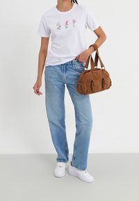 Hvid bomulds-T-shirt med blomsterbroderi, lyseblå denimjeans og brun kordfløjls-håndtaske med tre lommer, kombineret med hvide sneakers.