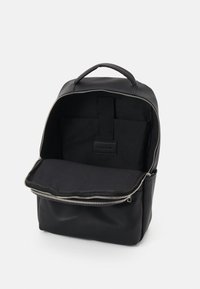 Sac à dos en nylon noir avec une texture lisse, comportant une fermeture éclair, une poche avant et une poignée renforcée. L'intérieur est doublé de tissu noir.
