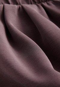 Pehme riie, millel on tekstuur, tuhm mauve värv, millel on voldid ja õrn riputus. Materjal tundub kerge ja sile.
