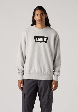 Grijze sweatshirt met een zwart "LEVI'S" logo aan de voorkant, voorzien van een ronde hals, geribbelde manchetten en een relaxte pasvorm. Gecombineerd met donkere cargo-broeken.