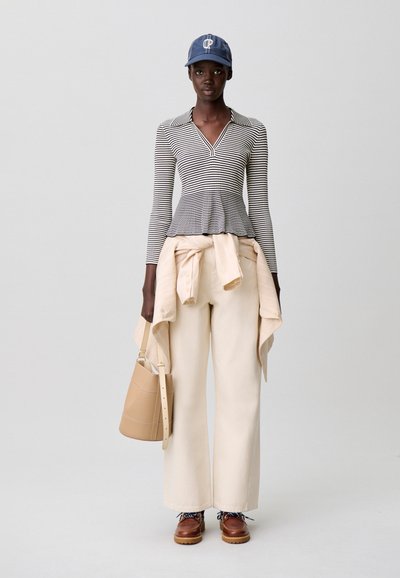 Camiseta de manga larga a rayas, pantalones beige de pierna ancha, suéter ligero atado a la cintura, bolso tipo cubo en color tostado, zapatos marrones con cordones, gorra azul con logo.