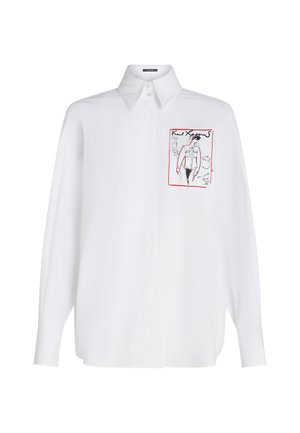 Witte langwerpige blouse met knoopsluiting en een puntige kraag. Heeft een bedrukt ontwerp op de borst in zwart en rood. Gladde textuur.