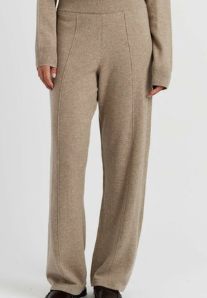 Beige gebreide broek met zichtbare naadlijnen, gedragen met bijpassende gebreide trui en donkere schoenen, getoond van taille tot voeten.