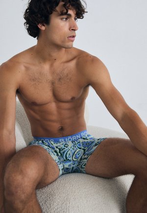 Par modrih in zelenih boxer šortih z vzorcem z elastičnim pasom, ki vsebuje besedilo "Björk Bong". Mešanica bombaža z gladko teksturo.