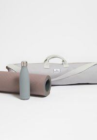 Esterilla de yoga en rosa suave, botella de agua de acero inoxidable en gris claro, y una bolsa de transporte gris con asas en contraste.