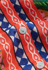 Červená a modrá vzorovaná látka s bielymi geometrickými vzormi a dvoma bielymi okrúhlymi gombíkmi prišitými pozdĺž vertikálneho švu.