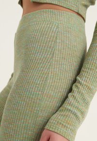 Leggings vert en tricot côtelé avec un motif texturé et des accents subtils de bleu et d'orange, au design ajusté et détails sur les coutures latérales.