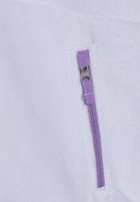 Tessuto in felpa bianca con superficie testurizzata. Presenta una cerniera viola e un tassello in tessuto, con cuciture visibili lungo i bordi.