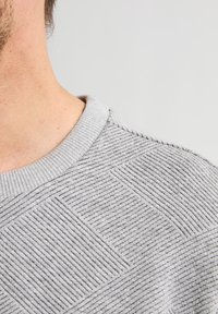 Grijze textuurtrui met een geribde kraag, subtiele diagonale en horizontale patronen voor visuele belangstelling en een zachte stoffen afwerking.