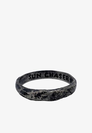 Tamsaus metalo žiedas su šiurkščia tekstūra, vidinėje pusėje matomas užrašas „SUN CHASER“.