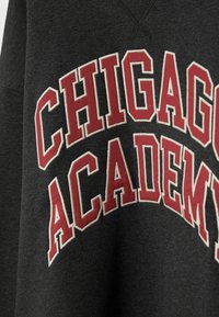 Tissu gris foncé avec un grand texte rouge et blanc en contour indiquant "CHICAGO ACADEMY" en forme d'arche.