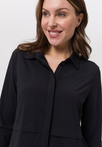 Schwarzes langärmliges Hemd mit Knöpfen und Kragen, das ein geschichtetes Design, eine glatte Textur und Knopfdetails auf der Vorderseite aufweist.