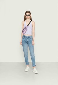 Top curto lilás, jeans de cintura alta azuis, ténis brancos. Acessório: mala de ombro com padrão roxo, óculos de sol pretos. Look simples e casual.