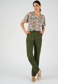 Top de manga corta con estampado floral en rojo, verde y blanco; combinado con pantalones relajados defit oliva y sandalias de cuña beiges.
