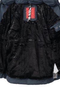Doublure en fourrure noire pelucheuse à l'intérieur d'une veste bleu marine avec une étiquette rouge et des étiquettes d'entretien attachées à l'intérieur.