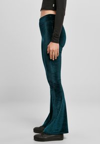 Tirkiznopoplave plišane hlače na zvono s glatkom teksturom i srednjim strukom, uparene s crnim tenisicama i uskom majicom s dugim rukavima.