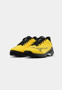 Des chaussures de sport jaunes avec des accents noirs, une tige texturée et des lacets noirs. La semelle extérieure présente un motif de semelle distinct pour une meilleure adhérence.