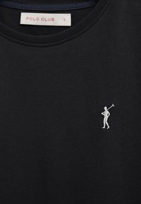Zwart shirt met ronde hals en een kleine witte geborduurde figuur die een polo-knuppel vasthoudt op de linkerborst, met een label "POLO CLUB" aan de binnenkant van de kraag.