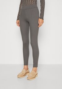 Grå leggings med en slät textur, en figursydd design och vertikala sömmar. Kombineras med beige mocka tofflor.