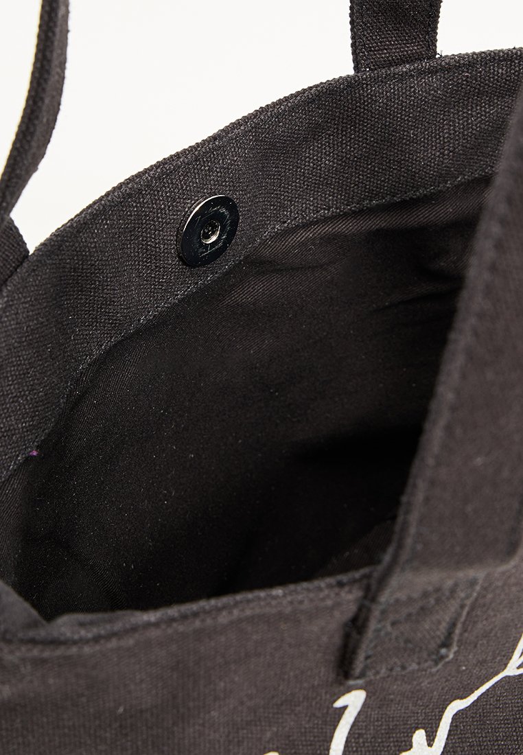 Bolso de lona negro con un acabado texturizado, que presenta un cierre de botón a presión y forro interior. Dos asas cortas de tela están unidas.