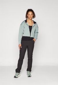 Giacca trapuntata azzurro chiaro con cappuccio, dettagli neri, chiusura con zip; abbinata a pantaloni neri e sneakers verde chiaro. Design minimalista.