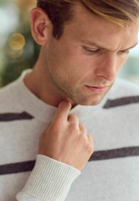 Light gray sweater with dark gray stripes, ribbed cuffs, and a round neckline. A hand touches the collar in a close-up shot.