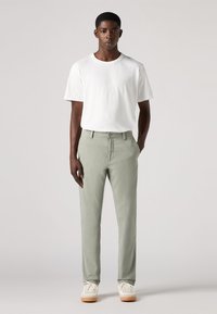 Pantaloni di cotone verde chiaro con vestibilità dritta, abbinati a una t-shirt bianca a girocollo e scarpe da ginnastica bianche con suole beige chiaro.