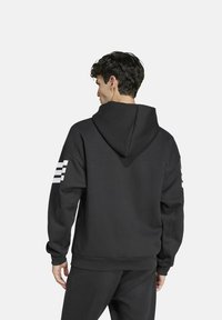 Felpa nera con cappuccio grande, caratterizzata da tre strisce bianche sulla manica sinistra, realizzata in tessuto morbido e con una vestibilità comoda.