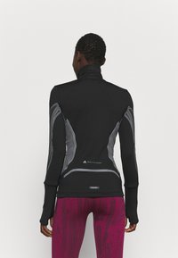 Black athletic top with a high collar, featuring grey accent lines and logo details. Made from a stretchy, fitted material.