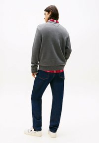 Gray knit sweater layered over a red plaid shirt, paired with dark blue jeans and white sneakers. Textured fabric and casual design.