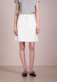 Valkoinen farkkuhame, puolipitkä, edessä napitus, yhdistettynä harmaaseen t-paitaan ja mustiin kenkiin, joissa on gingham-sidontakuvio.