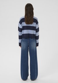 Maglione a righe blu e blu navy con un design cropped, abbinato a jeans di denim blu sbiadito a gamba larga. Il materiale appare morbido e casual.