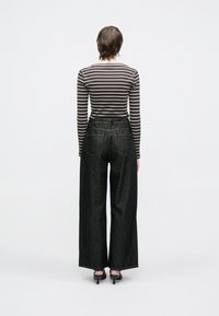 Melnas plašās kājas džinsi ar augstu vidukli, ar divām aizmugurējām kabatām un kontrastējošām šuvēm, kombinēti ar brūnu svītrainu garām piedurknēm krekliņu.