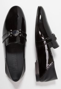 Chaussures en cuir verni noir à bout pointu, ornées d'un élément métallique décoratif et de deux brides horizontales sur le cou-de-pied.