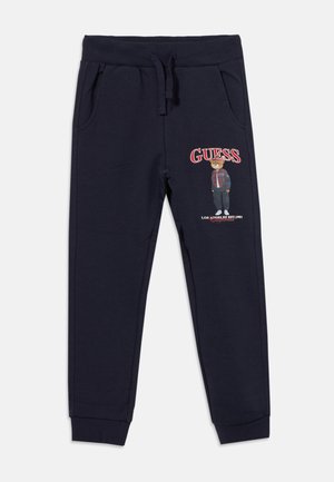Pantalon de survêtement bleu marine avec taille et poignets élastiques, doté de poches latérales et d'un ours imprimé portant des vêtements décontractés avec le texte "GUESS".