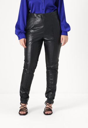 Black faux leather pants with a high waist, featuring stitch detailing and slim fit. Paired with a blue long-sleeve blouse and strappy sandals.