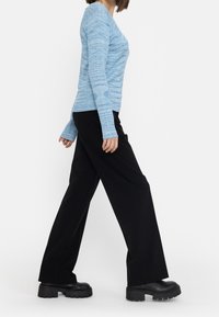 Ljusblå långärmad topp med ribbad textur och V-hals, ihop med svarta vida byxor och kraftiga svarta skor.