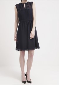 Vestito senza maniche blu navy con corsetto trasparente, scollatura a chiave, vita elastica e gonna fluida, abbinato a tacchi alti neri.