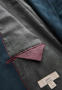 L'intérieur de la veste de costume marine présente une doublure à motif gris avec des accents bordeaux et une poche. L'étiquette indique "NEXT REGULAR FIT 38R."