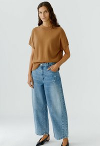 Bruine sweater met korte mouwen, relaxte fit, gecombineerd met lichtblauwe wijde jeans, met een vervaagde wasbeurt en zichtbare stikdetails.