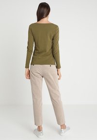 Olivgrünes Langarmoberteil mit Bootsausschnitt, kombiniert mit hellbeigen Cordhosen. Das Outfit wird von lässigen silbernen Sneakers ergänzt.
